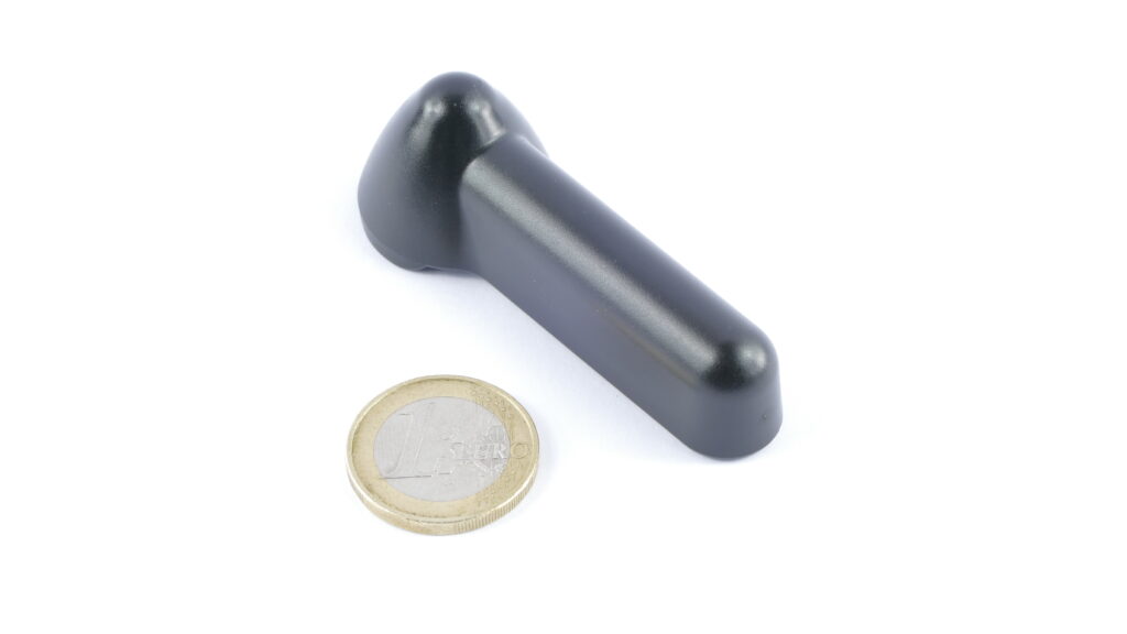 photographie d'un badge antivol à la forme allongé avec une pièce de 1€ à côté afin de comparer les tailles. Le badge fait environ 2 à 3 pièces.